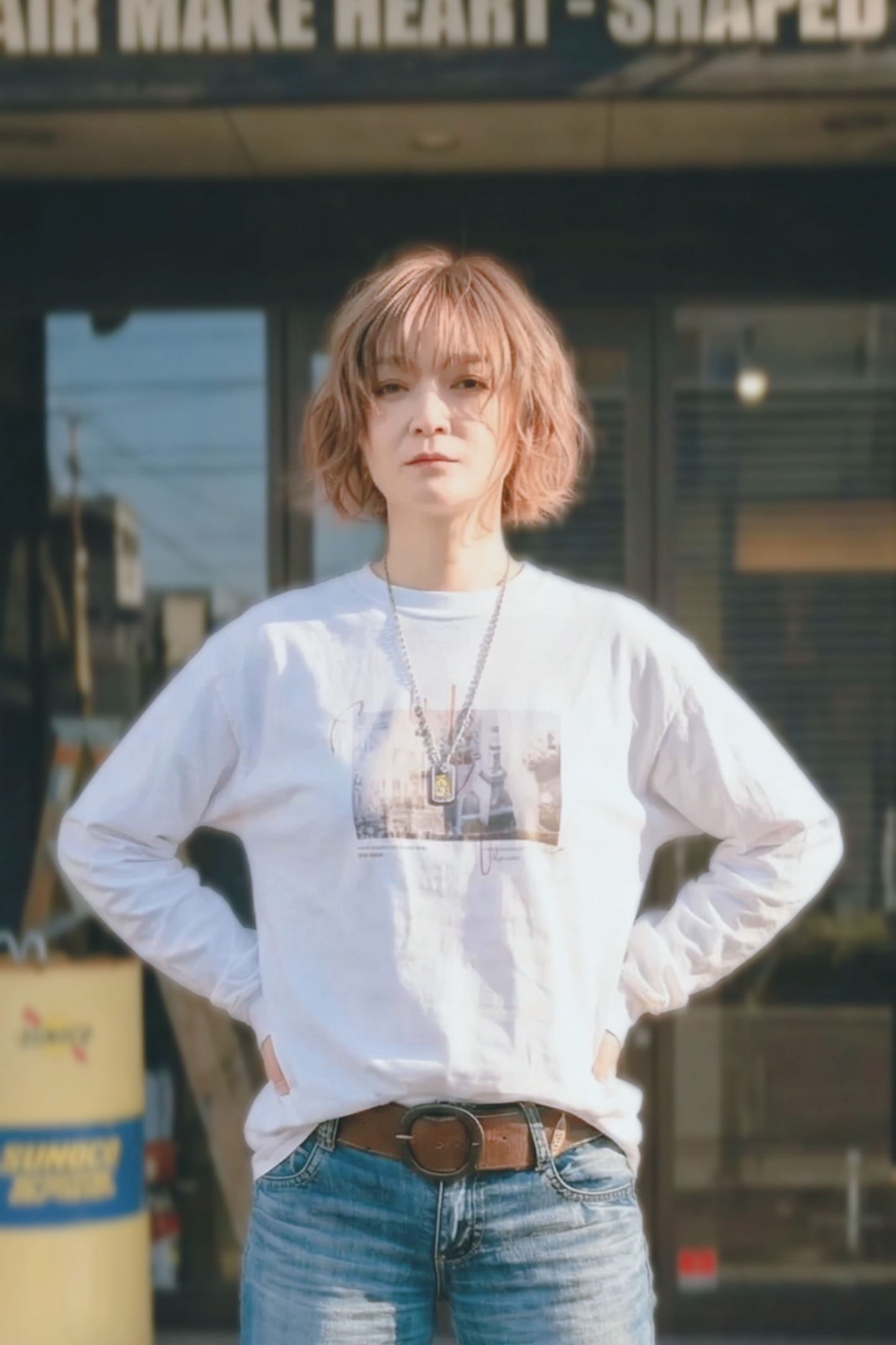 札幌市東区の美容室「ハートシェイプドボックス」のリケラトリートメント紹介イメージ。コンクリート壁を背景に、黒いベストと白いレースブラウスを着た女性が凛とした表情でカメラを見つめる。リケラで艶やかに整えられたダークブラウンの髪が、大人の女性の本質的な輝きを表現。