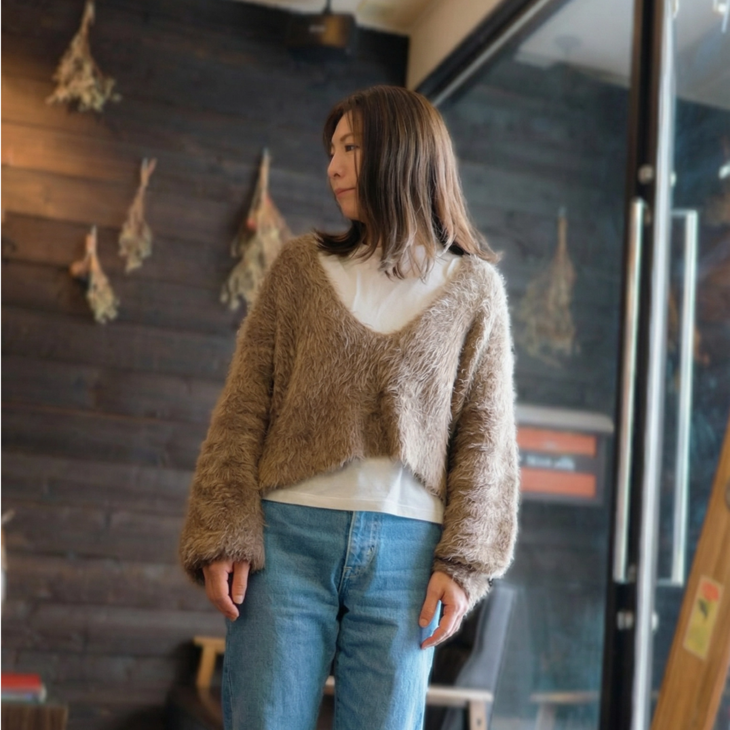 札幌市東区の美容室「ハートシェイプドボックス」のヘアスタイル作例。シンプルな白い壁を背景に、美しく整えられた髪に手をやる洗練された表情の女性。再現性の高いカットとカラー技術が光る一枚。